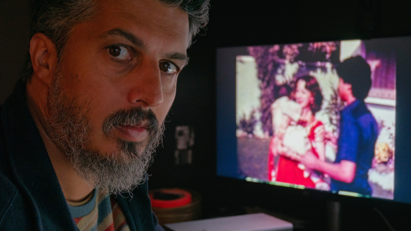 Director Sifian Khan turns to face the camera. Just over his shoulder, a TV screen shows a couple wearing bright colors.